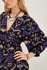 Vestido midi de viscosa con estampado estilo ikat en tonos oscuros, violetas y azules. Presenta mangas largas, cuello redondo y un diseño holgado que se ajusta a la cintura mediante un cinturón.