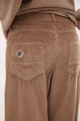 Pantalón de pana de corte ancho y tiro medio-bajo, con diseño de cinco bolsillos y acabado lavado. Presenta un aplique cuadrado decorativo en una de las piernas y un pin bordado de la marca.
