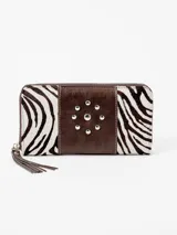 Billetera de cuero con cierre perimetral, diseño combinado con estampa animal print de cebra en los laterales y banda central de cuero marrón con tachas metálicas plateadas dispuestas en círculo. Incluye tiras de cuero colgantes en el tirador del cierre.