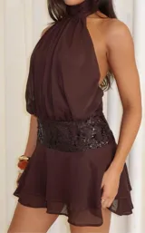 Vestido corto color marrón, con cuello halter, falda con volados y una faja central decorada con lentejuelas brillantes.