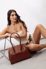 Cartera de mano estructurada de cuero vacuno rojo, con doble asa superior y detalles de charol en la parte superior. Cuenta con cierres metálicos y apliques decorativos laterales con hebillas.