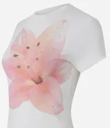 Remera baby tee de algodón color blanco, con cuello redondo, manga corta y un gran estampado frontal de una flor de lirio en tonos rosados con aplicaciones de pedrería.