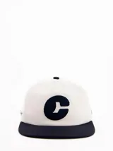 Gorra de béisbol blanca con visera plana azul marino y logo bordado en el frente.