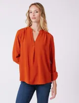 Blusa de gasa color beige, marca Floral & Ivy, con cuello a la base y escote en V. Las mangas son largas y regulables con presilla y botón.