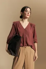 Camisa negra de manga larga con escote en V y cierre frontal de botones. Presenta detalles de volados en los hombros, frunces en la espalda y puños elastizados que le otorgan una silueta relajada y fluida.