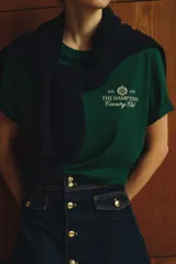 Remera de manga corta, cuello redondo y corte holgado, color verde oscuro, con estampado frontal en blanco que dice "EST. 1973 THE HAMPTONS Country Club".