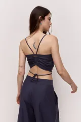 Blusa crop azul marino con tirantes finos y detalle de nudo frontal con forma de flor, con tiras para atar en la cintura.
