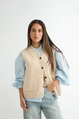 Chaleco de tejido de punto en color beige, con escote en V, cierre frontal con botones oscuros y dos bolsillos delanteros aplicados.
