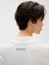 Top corto de punto acanalado color blanco, con cuello tipo chomba y cierre frontal abotonado.