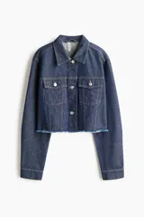 Campera cropped de denim de algodón rígido, color azul, con cuello, cierre frontal de botones metálicos, hombros caídos, bolsillos superiores con solapa y bajo deshilachado.