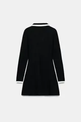 Vestido corto de tejido suave, color negro con detalles en blanco. Presenta cuello solapa, escote en pico, manga larga, falsos bolsillos delanteros y cierre frontal con botones dorados.