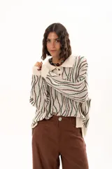 Buzo de tejido de punto con diseño de rayas verticales onduladas en tonos verde y marrón sobre base color crudo. Presenta cuello tipo polo con cierre frontal de botones y mangas largas con puños acanalados.
