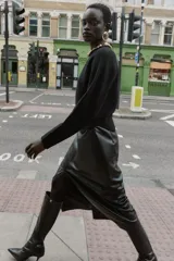 Jersey negro de cuello redondo con aplicación de bolas metálicas doradas, manga larga y bajo asimétrico. Cierre en la espalda con abertura y botón.