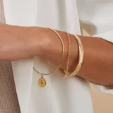 Esclava de alambre redondo en oro 9k, de diseño minimalista, con una medalla colgante que presenta un diseño grabado en forma de estrella con una circonia incrustada.