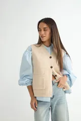 Chaleco de tejido de punto en color beige, con escote en V, cierre frontal con botones oscuros y dos bolsillos delanteros aplicados.