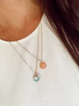 Collar de cadena fina de acero dorado con dije circular de piedra rosada.