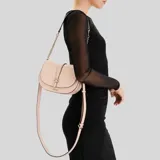 Cartera tipo saddle bag de Guess en color rosa, con estructura firme, solapa frontal con cierre de hebilla decorativa y logo metálico G. Incluye una correa de hombro con cadena metálica y detalles en cuero sintético.