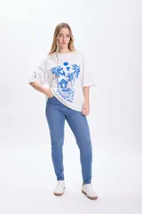 Remera blanca de corte amplio con estampado de palmeras, cabaña y aves en color azul.