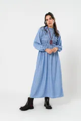 Vestido largo a rayas azules y blancas, con cuello alto fruncido, mangas globo con puños elásticos y cuerpo con detalle de nido de abeja hasta la cintura. Falda amplia de caída fluida.