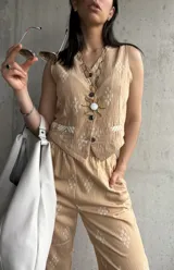 Chaleco beige con estampado de rombos blancos, cuello en V, cierre con botones y bolsillos delanteros ribeteados.