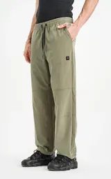 Pantalón de estilo cargo o técnico color verde militar, con cintura elástica ajustable con cordón negro y puños ajustados. Presenta costuras que simulan paneles y un pequeño logo cuadrado negro en el bolsillo lateral.