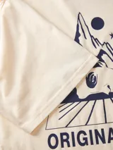 Remera color crema de algodón con cuello redondo y manga corta. Estampado con diseño abstracto en tonos azules, con la leyenda "Originals Studio Gallery District" y el número "1990".