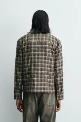 Camisa de corte relajado con estampado de cuadros en tonos marrones y blancos. Presenta cuello clásico, cierre frontal de botones, manga larga con puños abotonados y un bolsillo plastrón en el pecho.