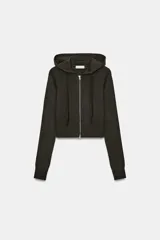 Sudadera cropped de punto con capucha ajustable mediante cordones, manga larga y cierre frontal con cremallera metálica. Presenta un diseño ajustado con acabados en rib en el ruedo y puños.