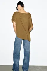 Top tipo capa blanco de punto fluido, con mezcla de viscosa, cuello bote, mangas cortas y bajo asimétrico.