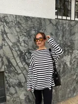 Conjunto compuesto por remera de manga larga oversize a rayas horizontales blancas y negras con escote bote, y pantalón negro de corte flared.