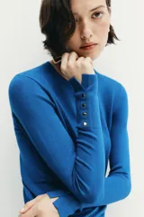 Jersey Zara de punto liso color negro, con cuello redondo, manga larga y detalle de botones dorados en los puños.