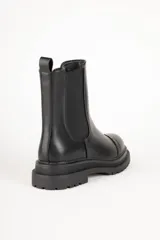 Bota Chelsea de cuero sintético color negro, con elástico lateral, puntera redondeada con detalle de perforaciones y suela track.