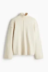 Buzo oversized de punto suave, color beige, con cuello alto acanalado y abertura posterior en V. Presenta hombros caídos, costuras decorativas verticales en el frente y terminaciones acanaladas en puños y bajo.