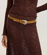 Cinturón estilo boho color tostado, con diseño de bordes ondulados y aplicaciones de tachas metálicas circulares. Cuenta con hebilla metálica de estilo western y múltiples perforaciones para ajuste.