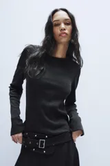 Vestido midi de cuello redondo y manga larga, confeccionado en tejido de punto gris oscuro. Presenta un cinturón integrado con hebilla y aplicación de tachas metálicas, y un bajo con diseño asimétrico y volados.
