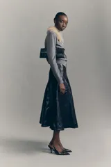 Cárdigan corto de punto fino color gris, con cuello desmontable de pelo sintético color beige. Presenta cierre frontal con botones y terminaciones acanaladas en puños y bajo.