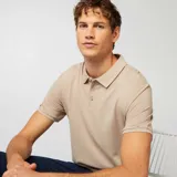 Remera polo de piqué de algodón color beige, con cuello clásico, manga corta y cierre de tres botones.