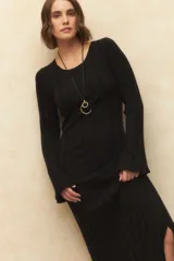Vestido largo de punto acanalado color negro, con corte ceñido al cuerpo, mangas largas acampanadas y aberturas laterales en el ruedo.