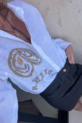 Camisa de lino color tostado, de manga larga y corte oversize, con bordado artesanal en hilo blanco en el frente y botones frontales.
