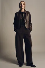 Pantalón de tiro medio color marrón oscuro con textura acanalada o plisada verticalmente. Presenta pierna ancha y cintura con trabillas.