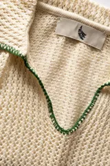 Polo de manga corta color crema de tejido calado, con cuello y escote en V con bordes en hilo verde oscuro. Confeccionada en algodón.