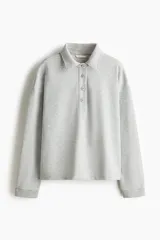 Buzo en tejido liviano color gris melange, con cuello camisero, tapeta con botones frontales, hombros caídos y puños acanalados.
