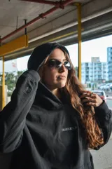 Canguro negro con capucha, corte oversize y diseño con hombros caídos. Presenta detalles bordados en la espalda con la palabra "Dual" en tipografía cursiva junto a texto descriptivo en tonos monocromáticos.