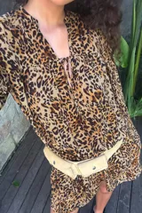 Vestido corto con estampado animal print, escote en pico con lazada ajustable, mangas largas abullonadas, cintura elástica y falda con volantes.