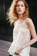 Top de encaje color crudo con escote recto y breteles finos ajustables. Modelo entallado con peplum levemente acampanado en tejido con brillo sutil.