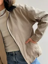 Campera de gabardina color beige con cierre frontal y cuello en contraste color negro. Presenta un diseño minimalista con bolsillos delanteros funcionales y calce cómodo.