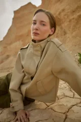 Chaqueta corta color beige de cuero sintético, con cuello alto, cierre frontal con botones a presión y bolsillos laterales con solapa.