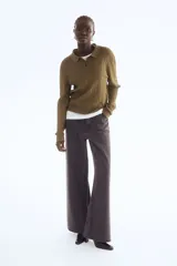 Sweater de punto color verde oliva, con cuello polo, tapeta de dos botones y manga larga. Presenta un tejido con diseño de trenzas verticales a lo largo del cuerpo y puños y bajo acanalados.