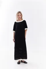 Vestido midi negro de tejido de punto de algodón, con mangas cortas, cuello redondo y terminaciones en color blanco en el cuello, mangas y ruedo. Presenta detalles geométricos perforados en la parte inferior de la falda y bordado sutil en el pecho.