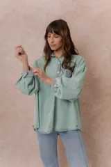 Camisa lila de calce relajado y manga larga, con cuello clásico, puños y bolsillo delantero en denim contrastante. Cierre frontal con broches metálicos.